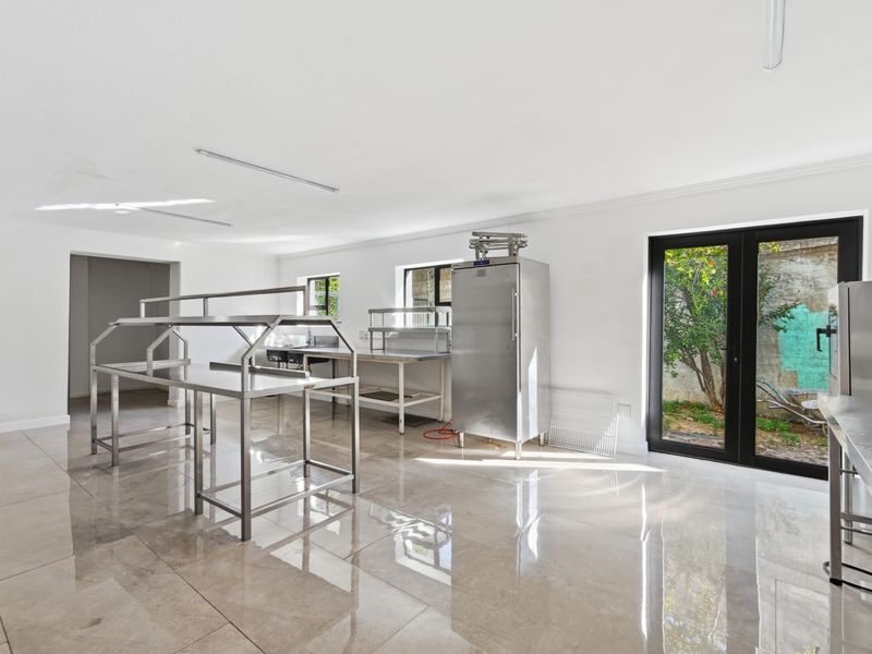 A clean, commercial-style kitchen space featuring stainless steel prep stations, a large refrigerator, polished tile flooring, and direct access to an outdoor area.