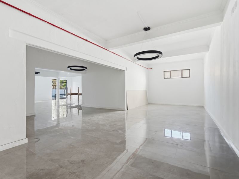 Spacious open-plan office area featuring polished porcelain flooring, modern circular pendant lighting, and exposed fire safety infrastructure.