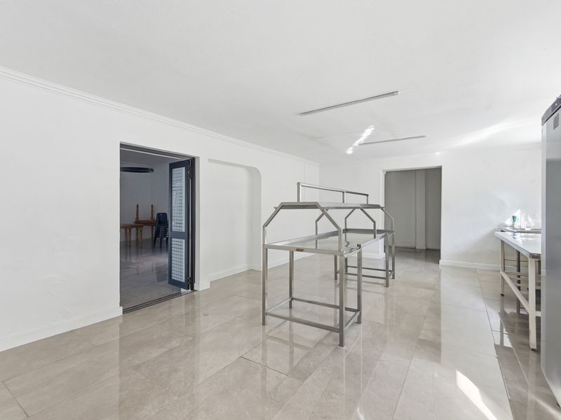 A spacious, minimalist kitchen area featuring polished tiled flooring, stainless steel prep stations, and clean white walls, suitable for a professional office environment.