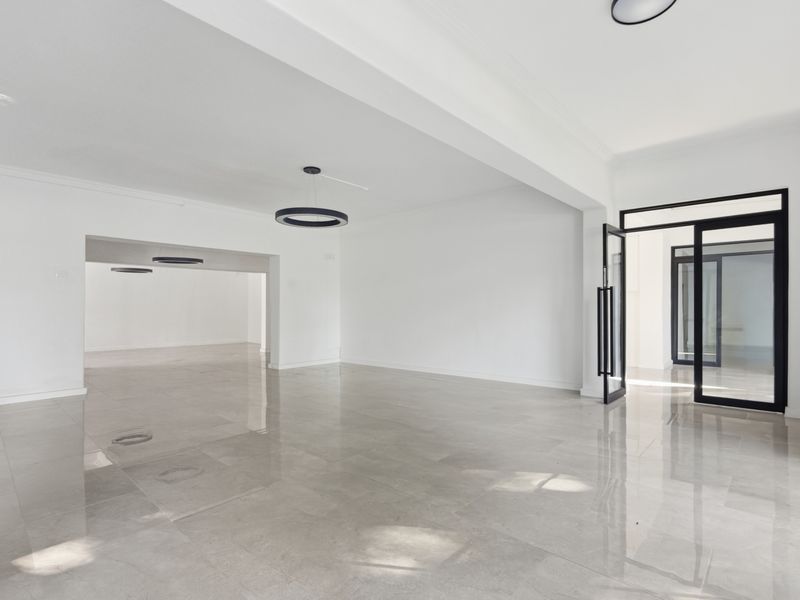 Spacious, modern open-plan office area featuring polished tile flooring, contemporary circular pendant lighting, and sleek black-framed glass entry doors.