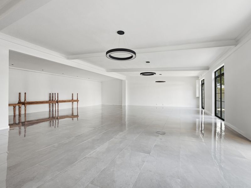 Spacious open-plan office area featuring polished large-format floor tiles, modern circular pendant lighting, and black-framed glass doors providing ample natural light.