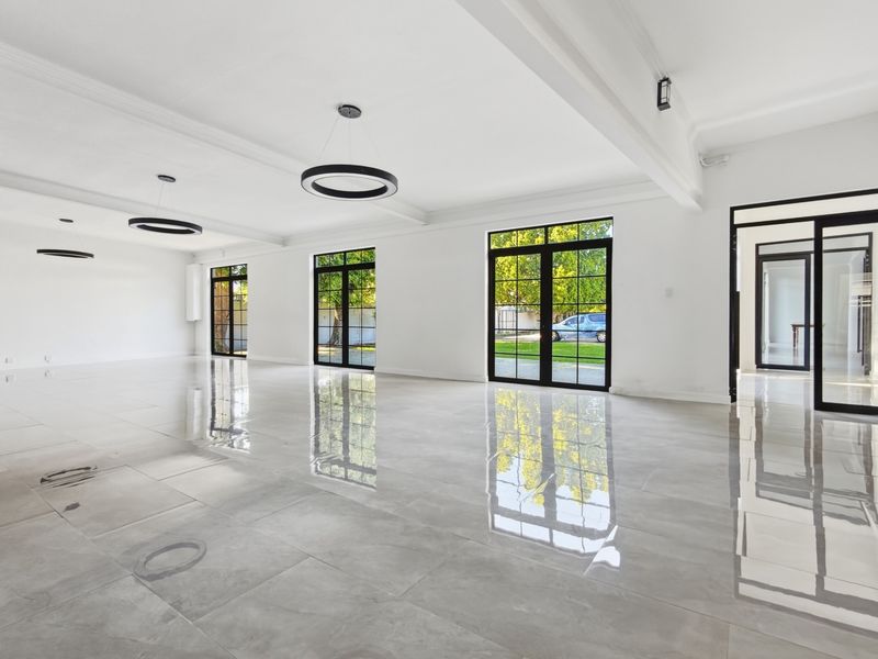 Spacious, modern office area featuring polished large-format floor tiles, black-framed glass doors, and contemporary circular pendant lighting in a bright, open-plan layout.