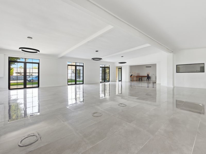 Spacious open-plan office area featuring polished large-format floor tiles, black-framed glass doors, and modern recessed ceiling details with contemporary pendant lighting.