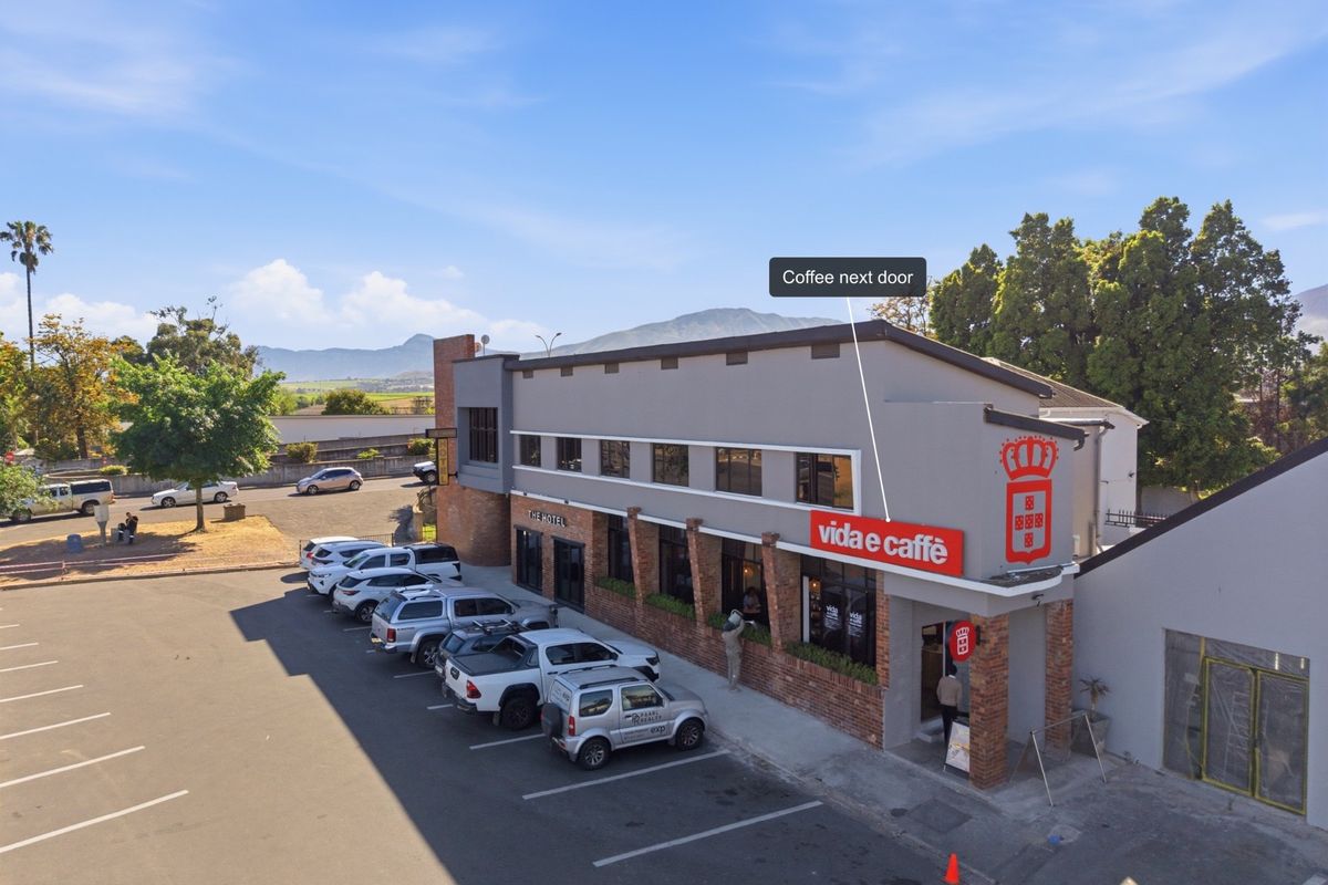 Aerial view of a commercial office building featuring a paved parking area and prominent street-level retail signage.