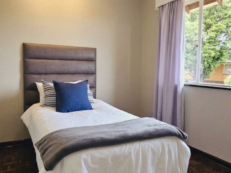 A well-maintained bedroom featuring classic parquet flooring, neutral wall tones, and modern track lighting, offering a comfortable and inviting living space.