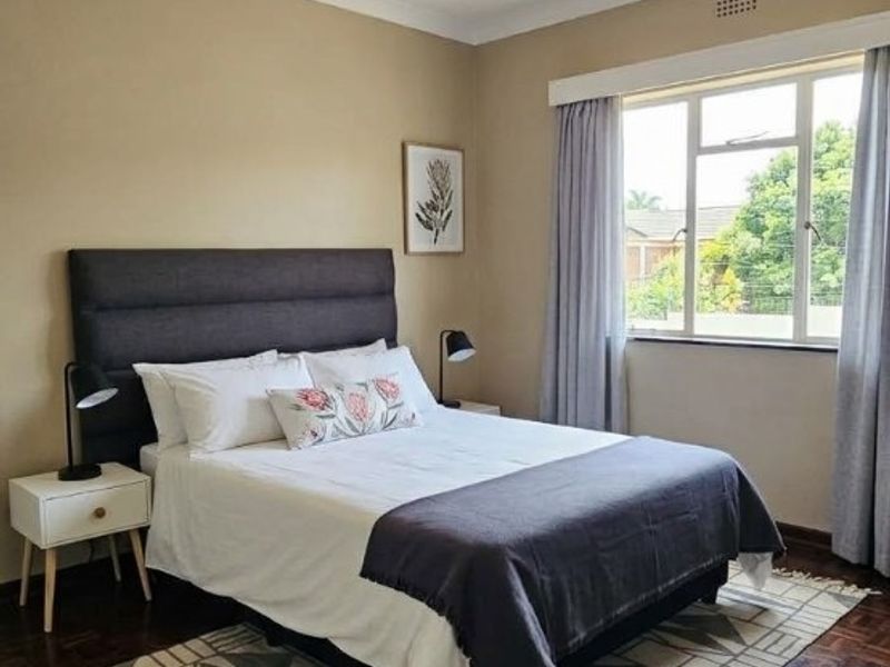 A well-maintained bedroom featuring classic parquet flooring, neutral wall tones, and a large window that provides ample natural light.