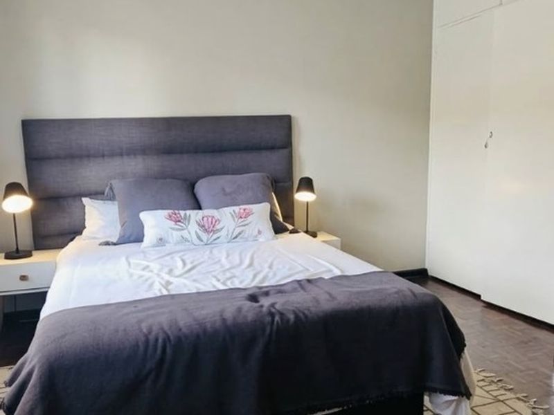 A well-maintained bedroom featuring classic parquet flooring, neutral wall finishes, and ample built-in cupboard storage.