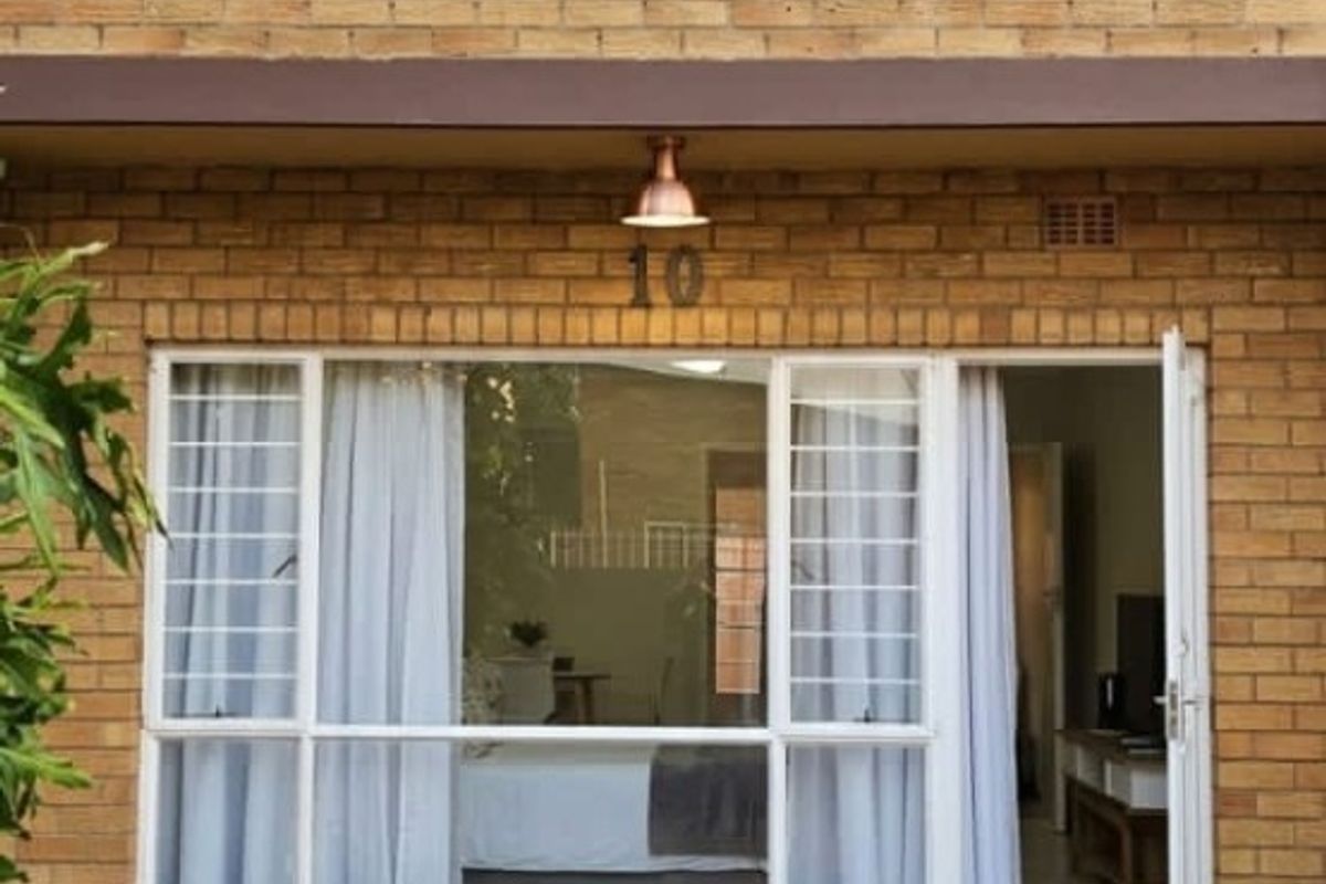 Rear exterior view of the apartment featuring a face brick facade, stone paved patio, and large windows with security bars.
