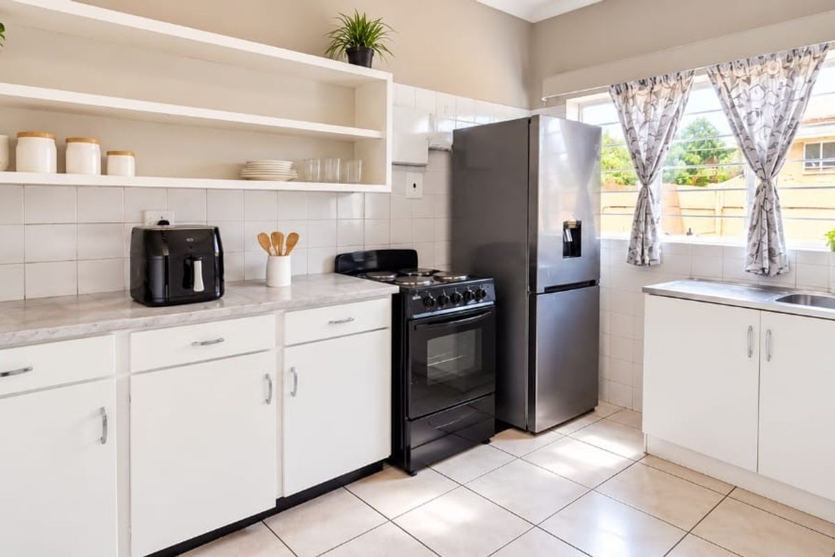 A functional kitchen featuring white cabinetry, open shelving, tiled backsplash, and a freestanding oven, providing a clean and practical workspace.