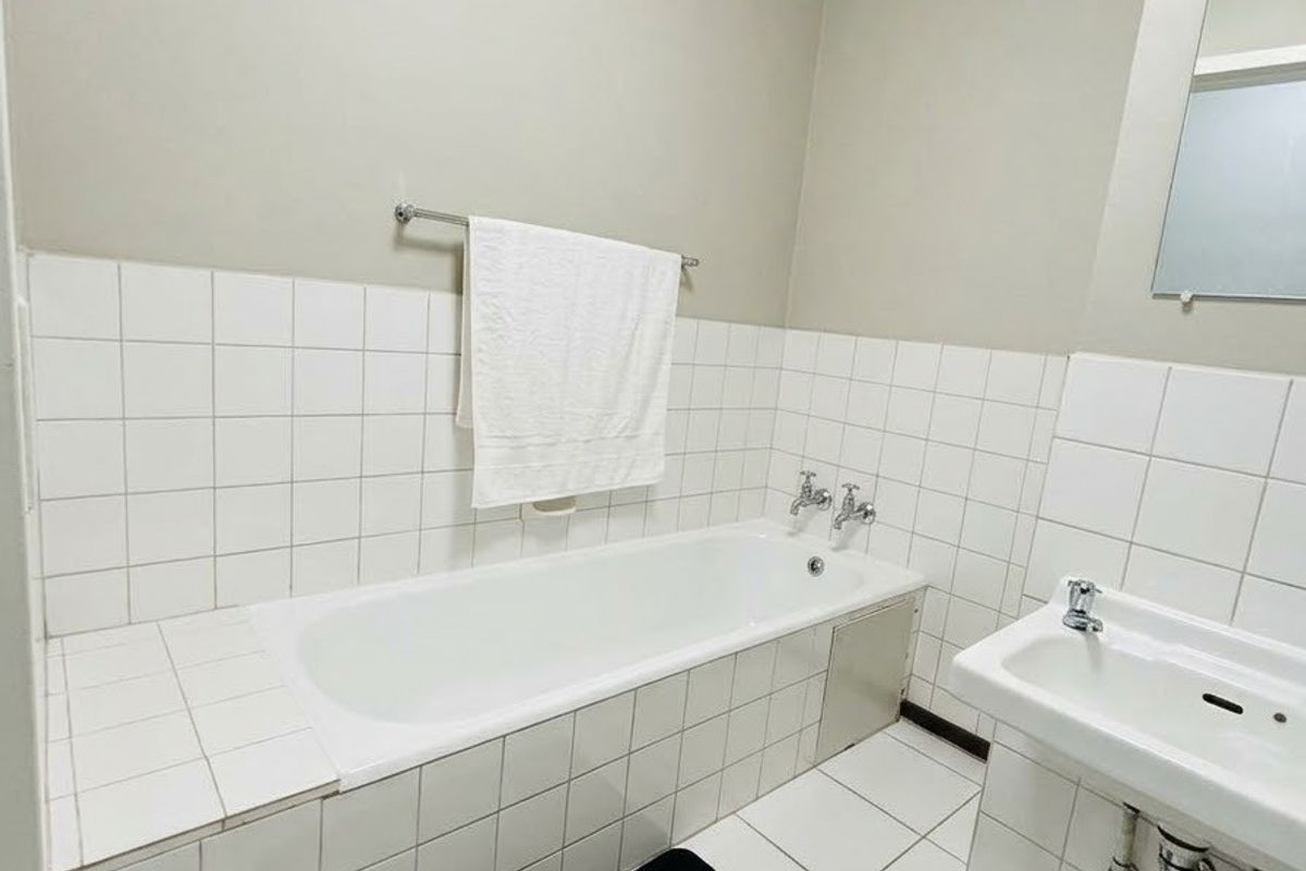 A functional bathroom featuring a built-in bathtub, wall-mounted basin, and white tiled finishes throughout.