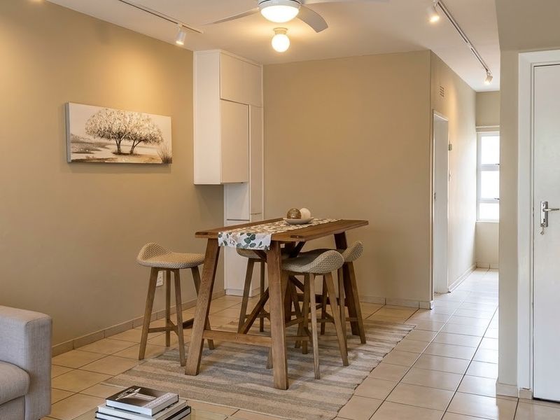 An open-plan living and dining area featuring neutral wall tones, tiled flooring, track lighting, and a ceiling fan, creating a functional and cohesive living space.