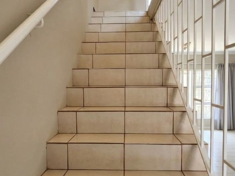 A clean, well-lit staircase featuring neutral floor tiles, a white metal balustrade, and a modern recessed ceiling light.