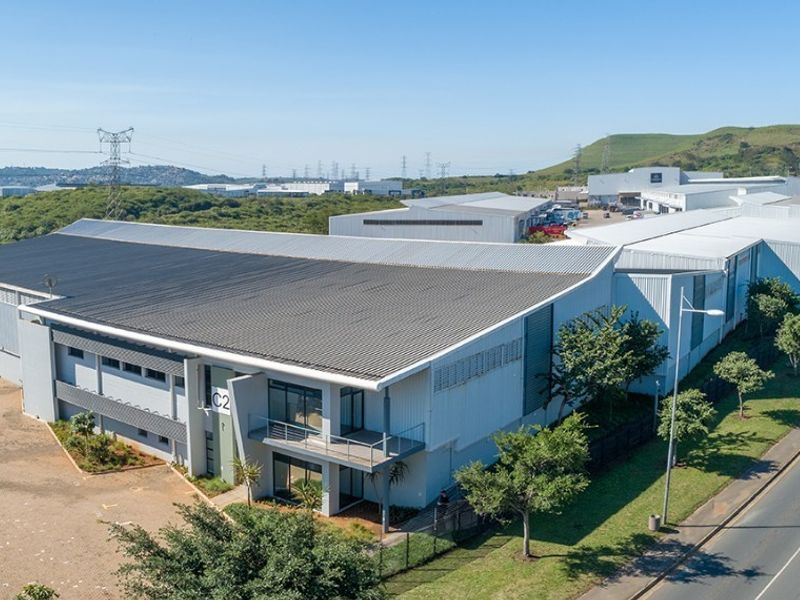 Aerial view of a modern commercial warehouse facility featuring a large metal roof, integrated office balcony, and paved parking area.
