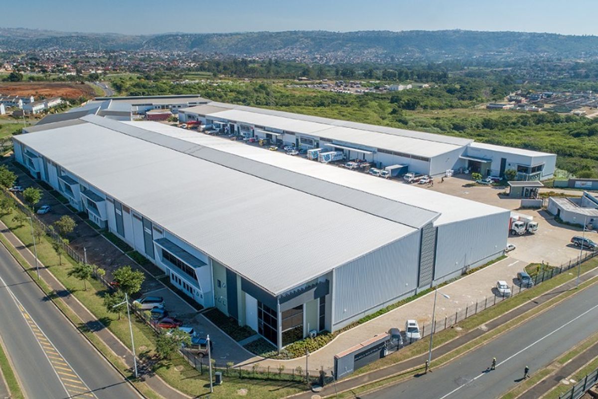 Aerial view of a large commercial industrial warehouse complex featuring extensive metal roofing, loading bays, and secure perimeter fencing.