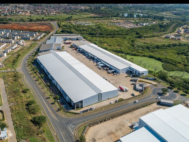 Aerial view of a large commercial industrial warehouse complex featuring extensive metal roofing, paved loading yards, and direct access to main road infrastructure.