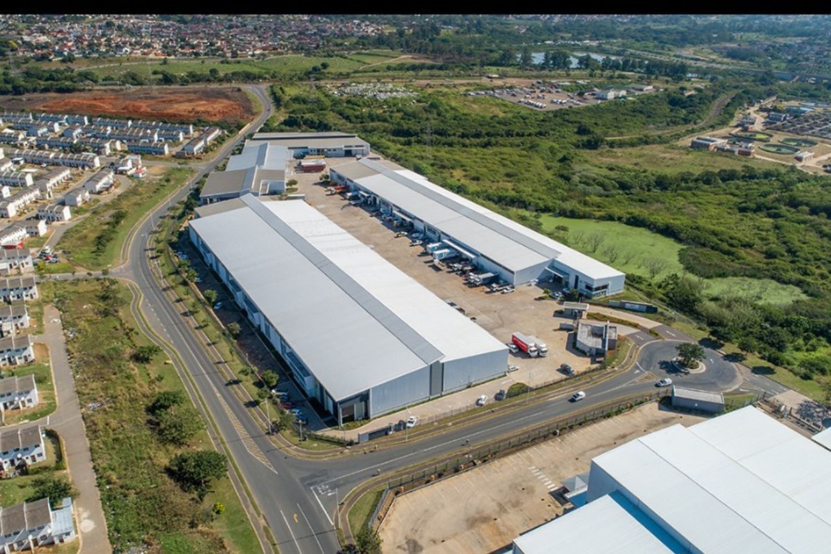 Aerial view of a large commercial industrial warehouse complex featuring extensive metal roofing, paved loading yards, and direct access to main road infrastructure.