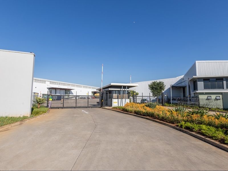 Commercial property entrance featuring a secure gated access point, guard house, and well-maintained concrete driveway leading to industrial warehouse facilities.