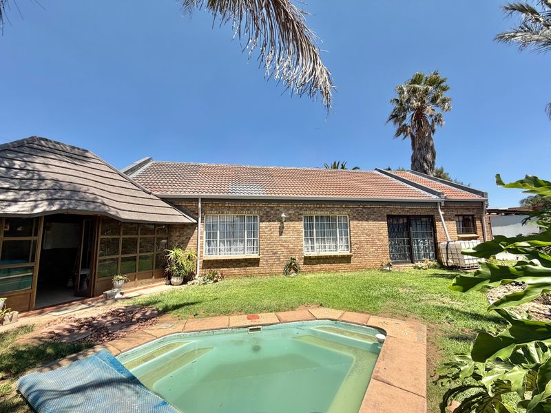 Rear view of a brick house featuring a swimming pool, a lawn area, and a combination of tiled and thatched roof sections.