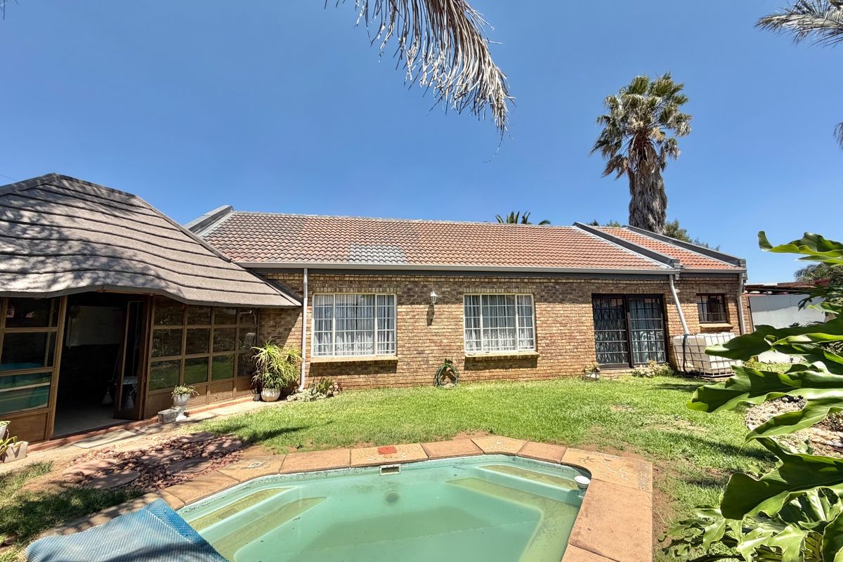 Rear view of a brick house featuring a swimming pool, a lawn area, and a combination of tiled and thatched roof sections.