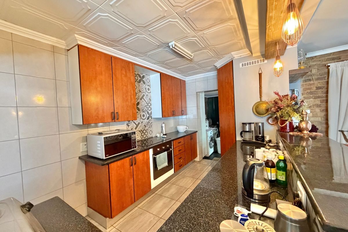 A functional kitchen featuring warm-toned cabinetry, granite countertops, a breakfast bar, and decorative ceiling tiles, with an adjacent laundry area visible.