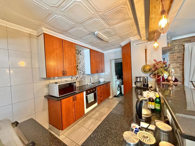 A functional kitchen featuring warm-toned cabinetry, granite countertops, a breakfast bar, and decorative ceiling tiles, with an adjacent laundry area visible.