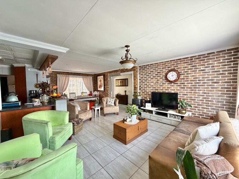 Spacious open-plan living area featuring a prominent exposed brick wall, tiled flooring, and a functional kitchen island with integrated lighting.