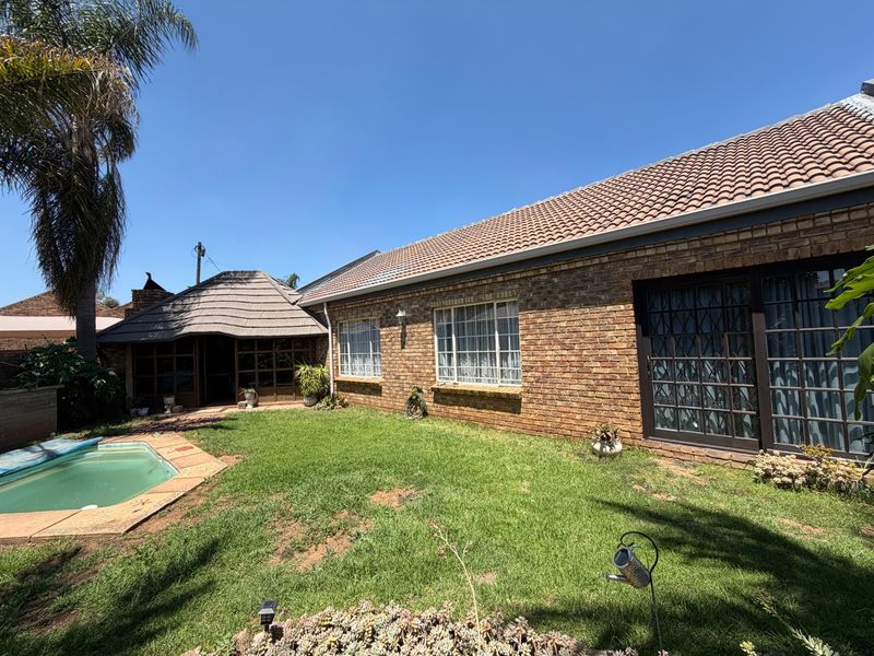 Rear view of a face brick house featuring a tiled roof, swimming pool, and a lapa area set within a private garden.