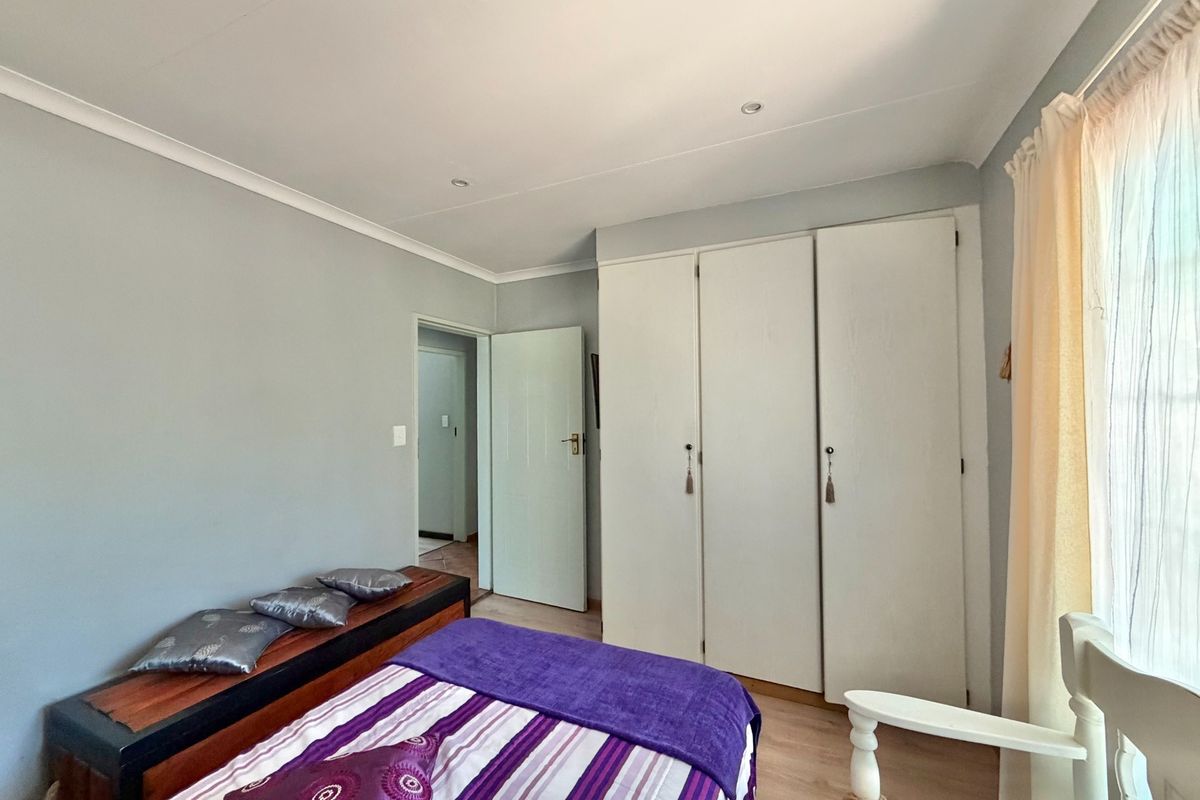 A well-maintained bedroom featuring built-in cupboards, laminate flooring, and recessed downlighting, offering a clean and functional living space.