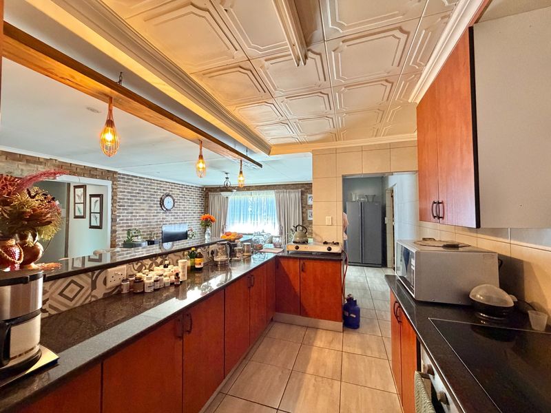 Spacious open-plan kitchen featuring granite countertops, warm wood cabinetry, and a distinctive coffered ceiling, seamlessly flowing into the adjacent living area with exposed brick.