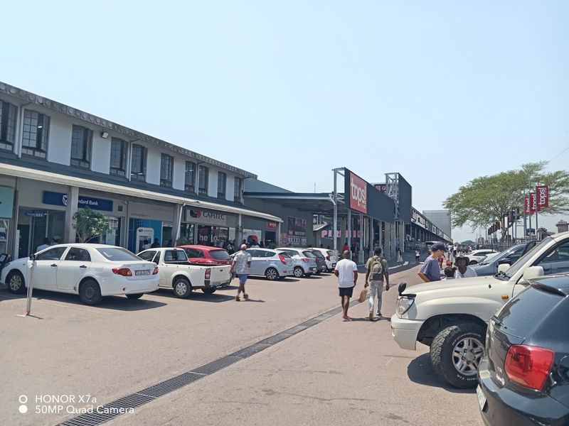 Exterior view of a retail shopping center featuring multiple storefronts, paved parking area, and building signage.