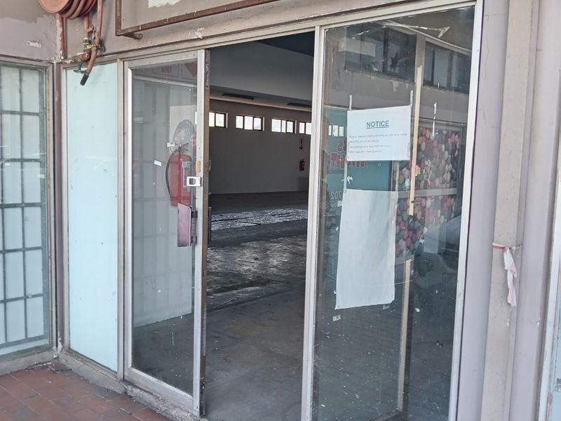 Front entrance of a retail space featuring a sliding glass door, fire safety equipment, and visible exterior wall wear.