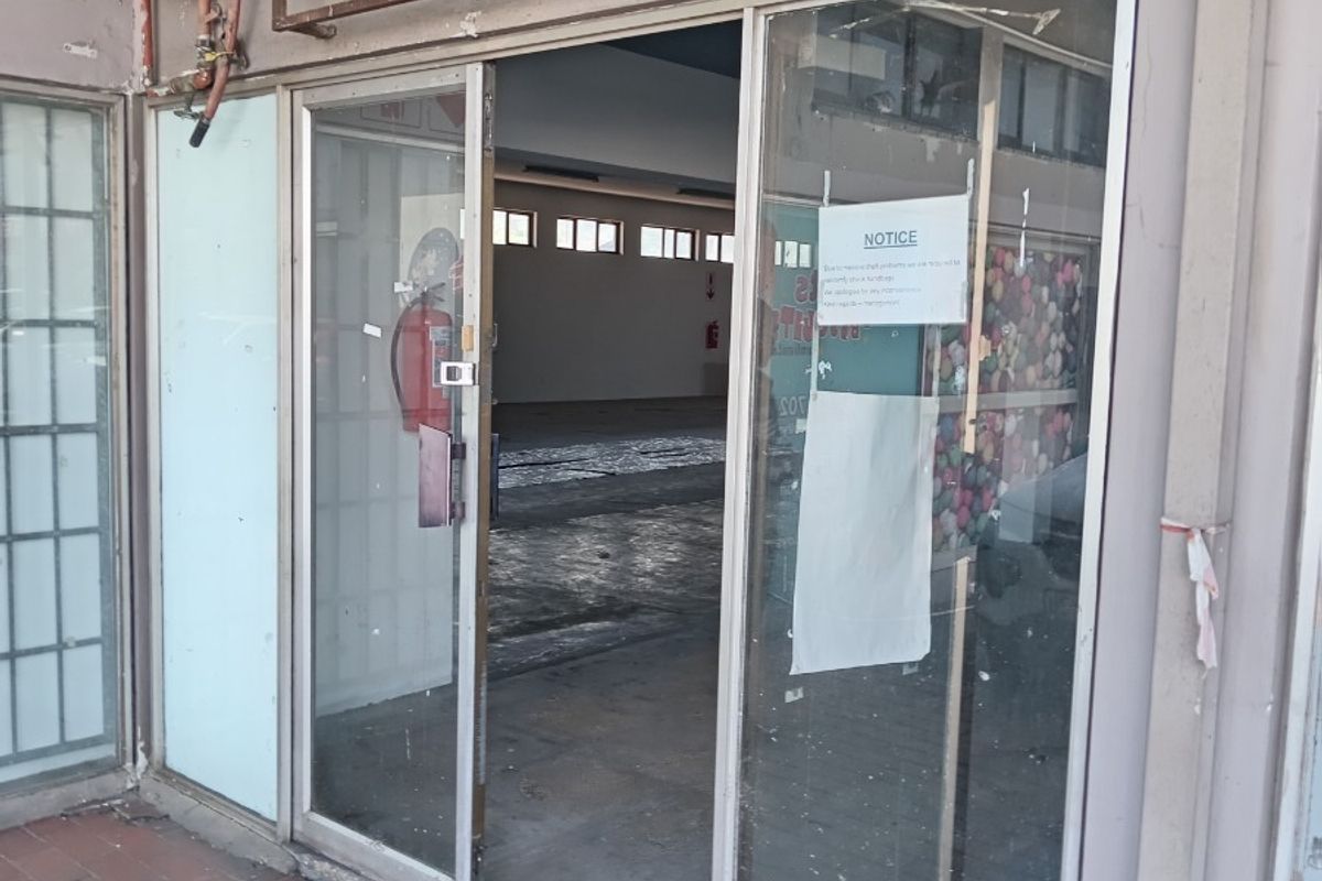 Front entrance of a retail space featuring a sliding glass door, fire safety equipment, and visible exterior wall wear.