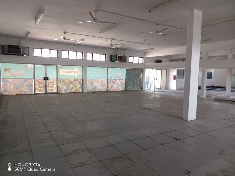 Spacious open-plan retail area featuring large glass storefront windows, tiled flooring, ceiling fans, and structural support columns, suitable for various commercial business layouts.