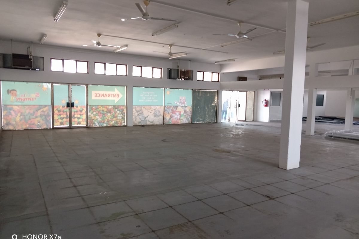 Spacious open-plan retail area featuring large glass storefront windows, tiled flooring, ceiling fans, and structural support columns, suitable for various commercial business layouts.