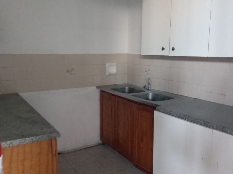 A functional, empty kitchen space featuring built-in wooden and white cabinetry, laminate countertops, a double bowl sink, and tiled backsplash and flooring.