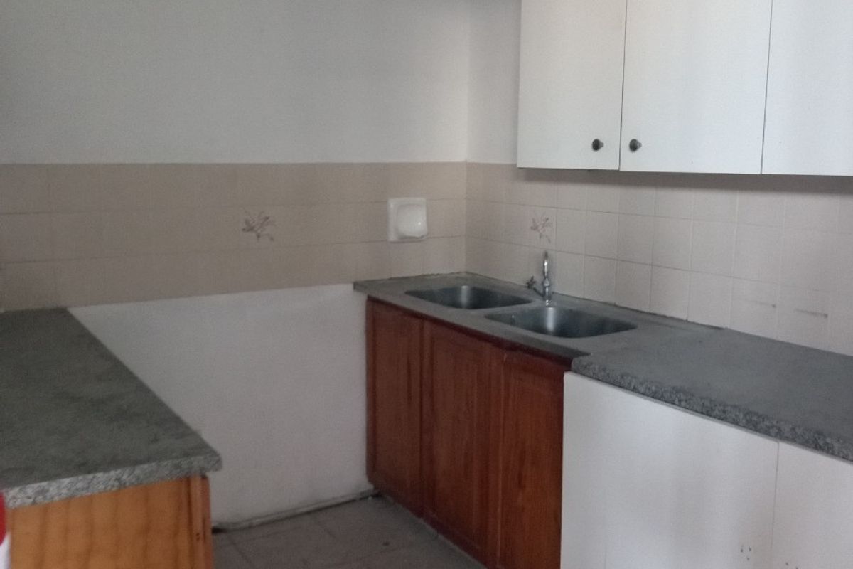 A functional, empty kitchen space featuring built-in wooden and white cabinetry, laminate countertops, a double bowl sink, and tiled backsplash and flooring.