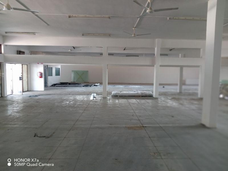A large, open-plan retail space featuring tiled flooring, structural columns, ceiling fans, and overhead fluorescent lighting, currently in a vacant shell condition.
