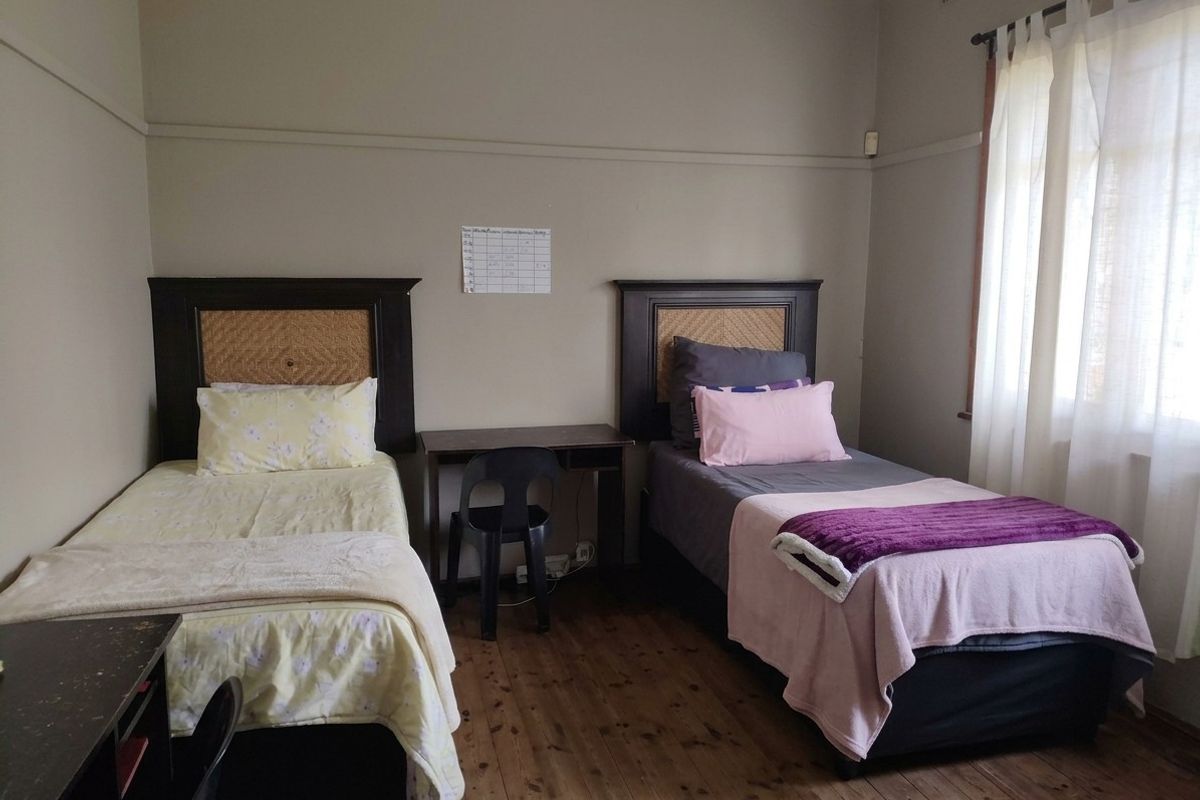 A bedroom featuring timber flooring and a picture rail, with natural light provided by a window with curtains.