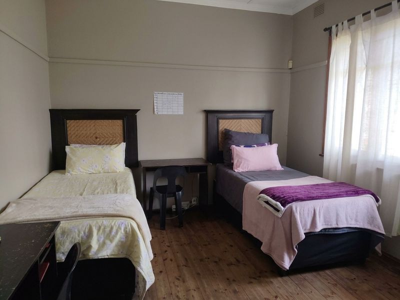 A bedroom featuring timber flooring and a picture rail, with natural light provided by a window with curtains.