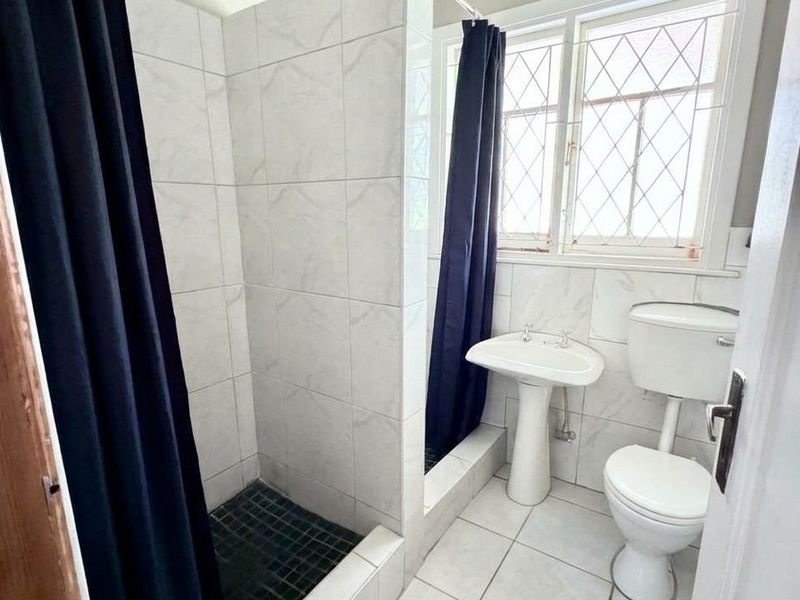 A functional bathroom featuring a walk-in shower with tiled surround, a pedestal basin, and a toilet, complemented by a leaded glass window.