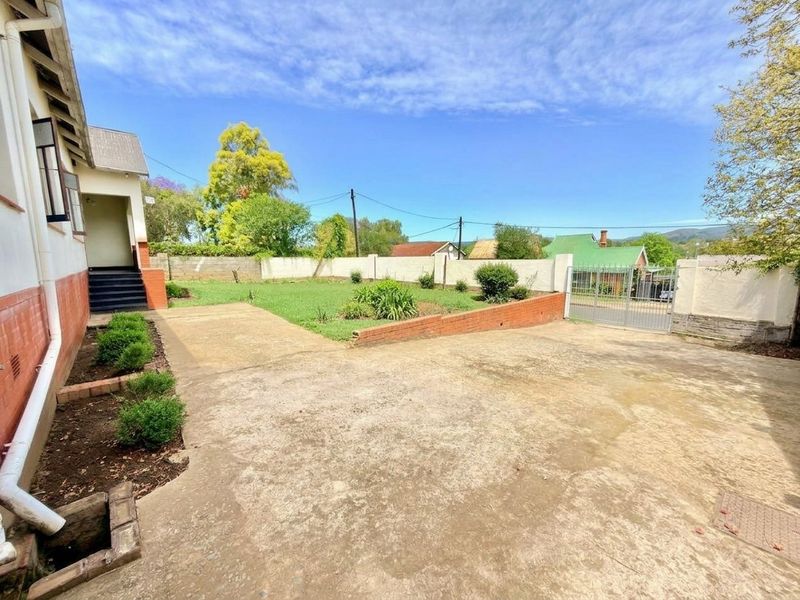 A spacious rear yard featuring a large concrete driveway, brick retaining wall, and perimeter boundary wall with a metal gate.
