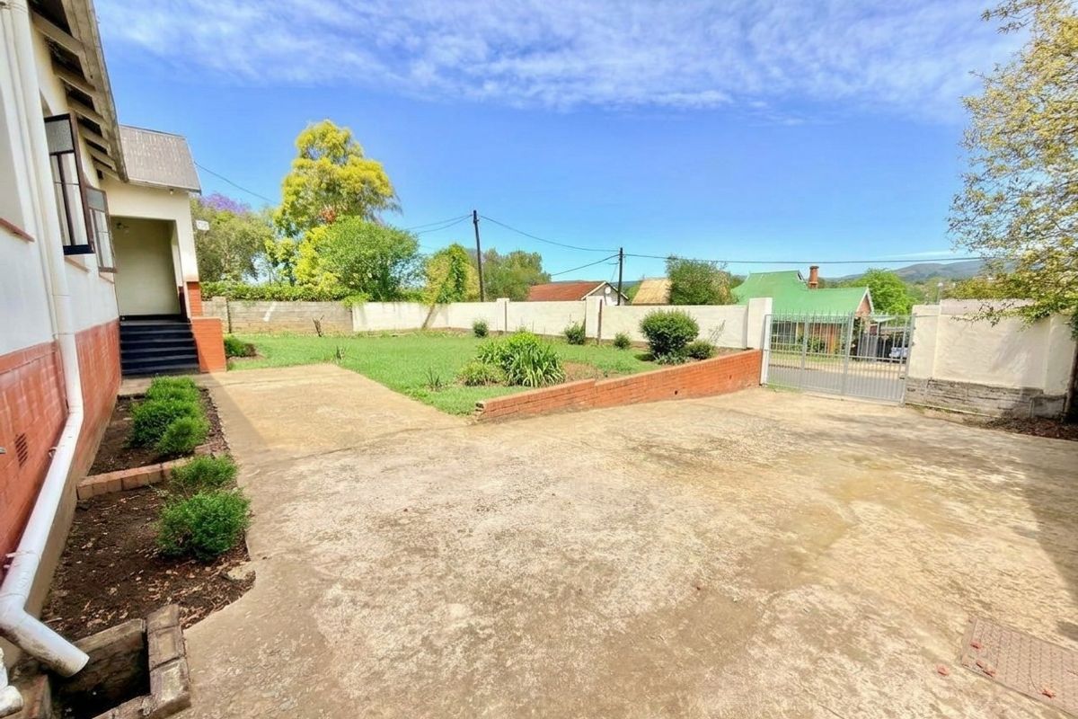 A spacious rear yard featuring a large concrete driveway, brick retaining wall, and perimeter boundary wall with a metal gate.