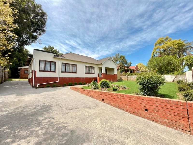 Front elevation of a single-story house featuring a concrete driveway, brick retaining wall, and a covered entrance porch set within a landscaped garden.