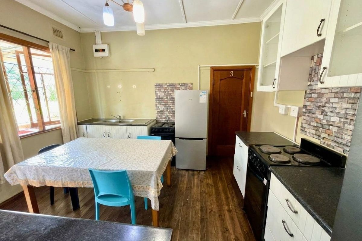 A functional kitchen featuring built-in cabinetry, a double sink, and an electric stove, with laminate flooring and a tiled backsplash.