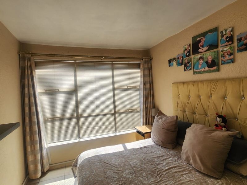 A bedroom featuring tiled flooring and a large window with venetian blinds, providing natural light to the space.