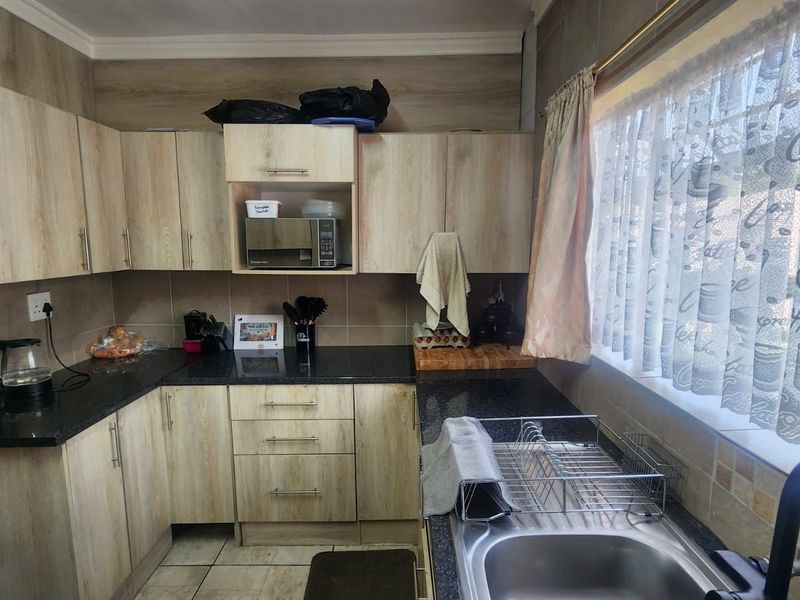 A functional kitchen featuring light wood-look laminate cabinetry, dark granite countertops, a stainless steel sink, and tiled backsplash with ample natural light.
