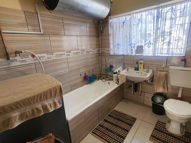 A compact bathroom featuring tiled walls, a bathtub, a wall-mounted basin, and a toilet, with an exposed water heater tank.