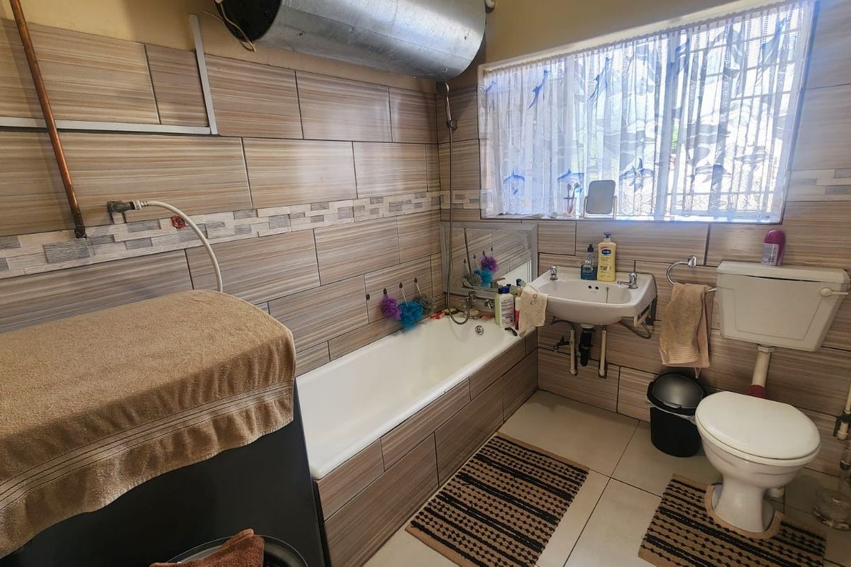 A compact bathroom featuring tiled walls, a bathtub, a wall-mounted basin, and a toilet, with an exposed water heater tank.