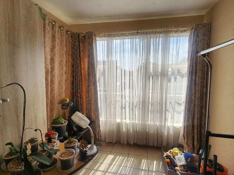 A living area featuring tiled flooring and a built-in cupboard, with large windows allowing for natural light.