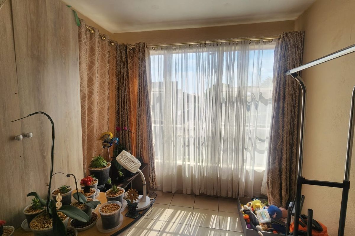 A living area featuring tiled flooring and a built-in cupboard, with large windows allowing for natural light.